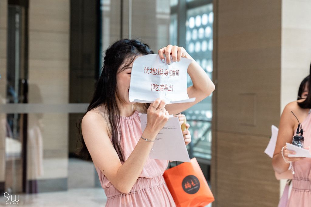 Bridesmaid in pink dress holds up sign during wedding celebration.