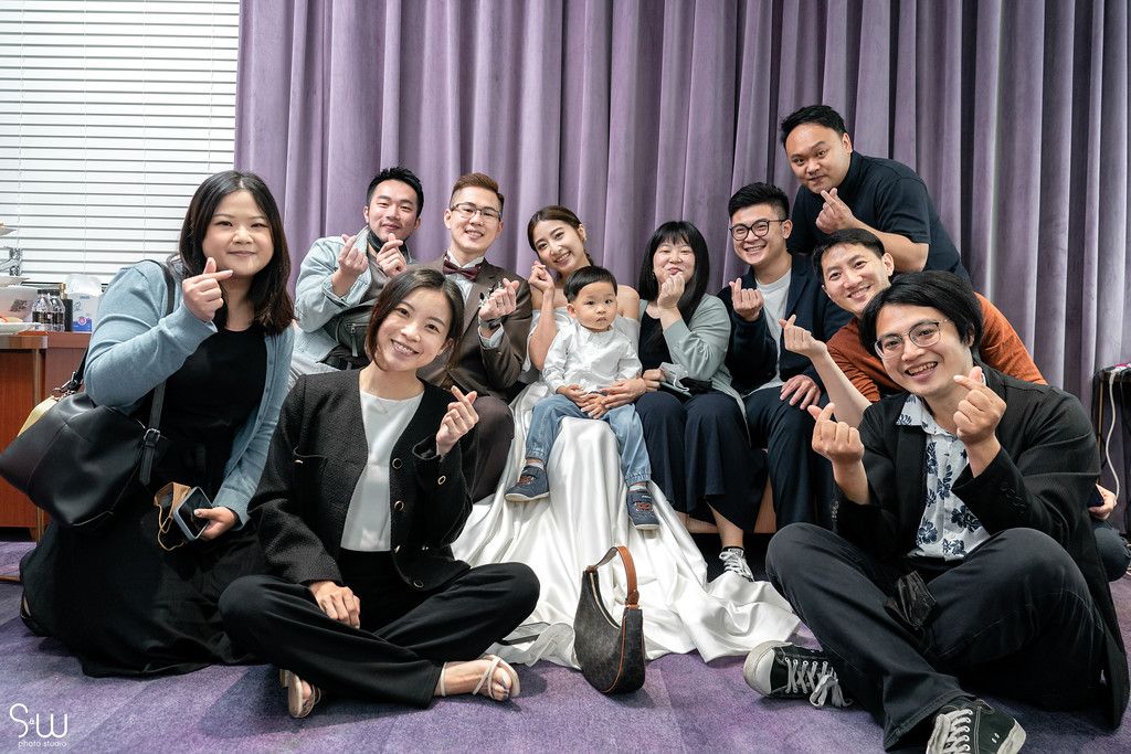 A celebratory group photo with wedding party members posing together on purple carpet.