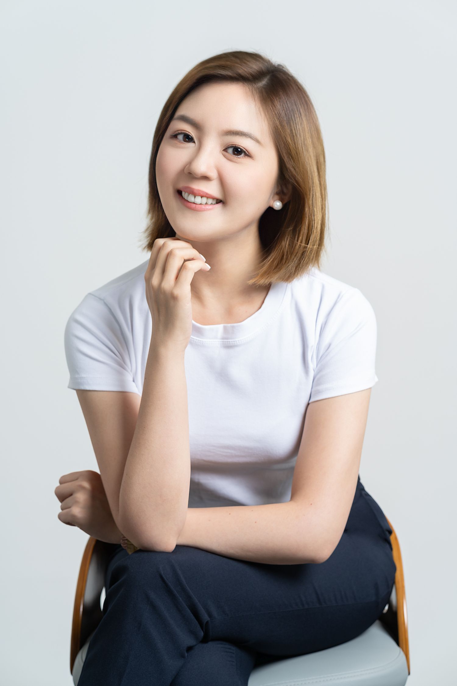 Person with short brown hair wearing a white t-shirt sits casually in a chair against white background.