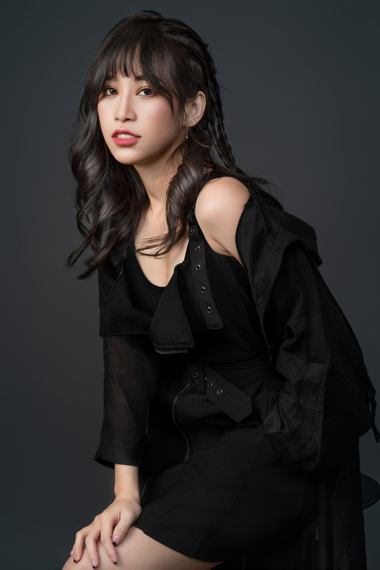 Professional studio portrait of a person in an elegant black outfit with flowing sleeves against a dark background.