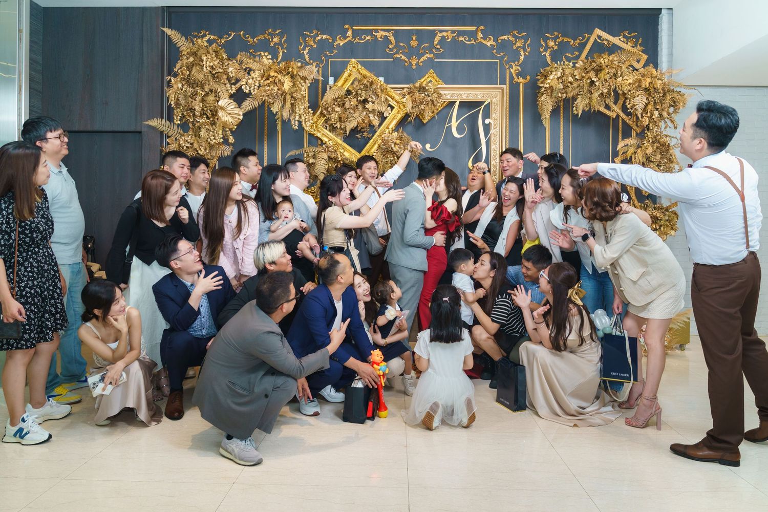 A large group of photographers gather at an event with cameras pointed towards a decorative golden backdrop.