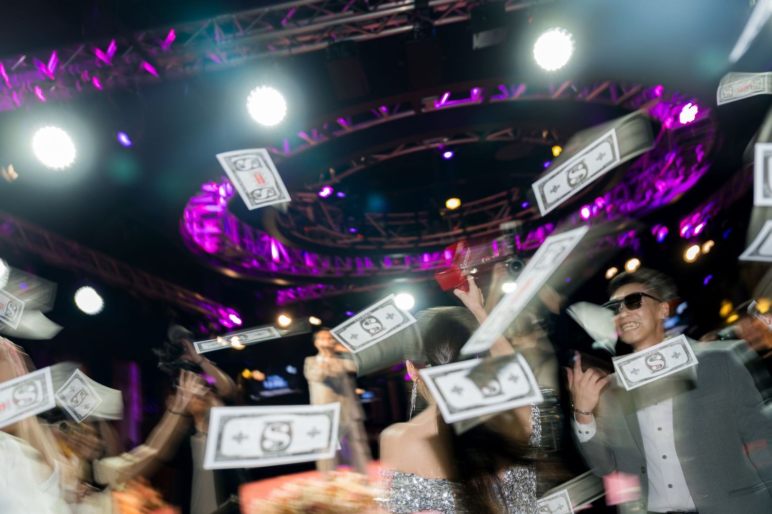 Cash money raining down on a dance floor with purple nightclub lighting and bright spotlights illuminating the scene.