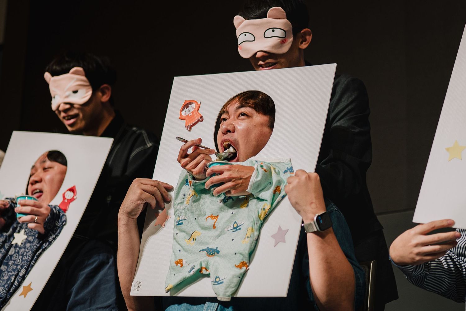 Three people wearing animal masks hold large portrait paintings at a creative art event.