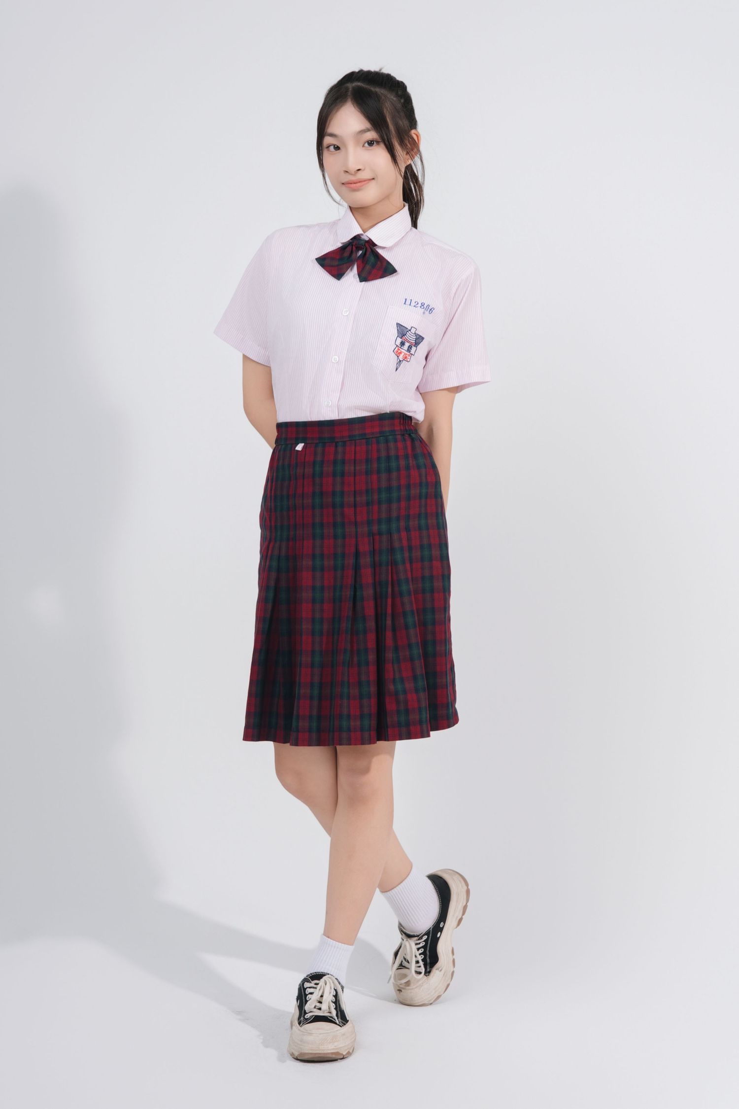 A student in a school uniform with a plaid pleated skirt and white polo shirt poses in different angles against a white background.