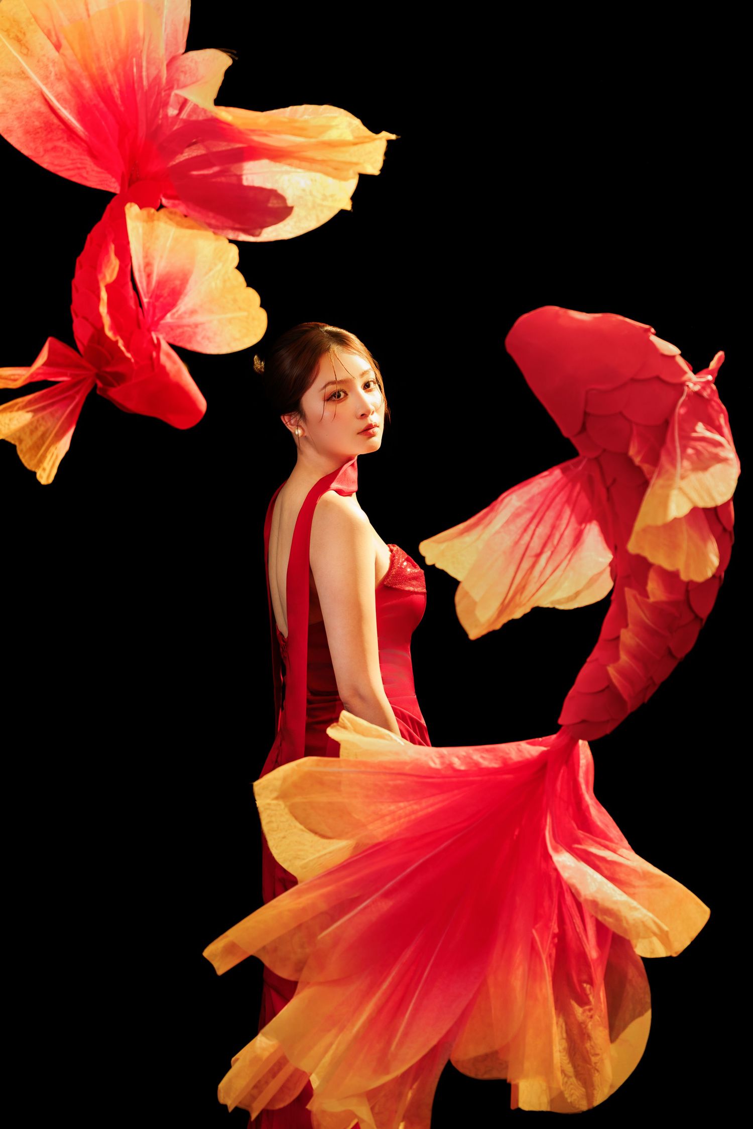 Woman in flowing red and yellow gradient gown poses gracefully against black background with dramatic fabric swirls.