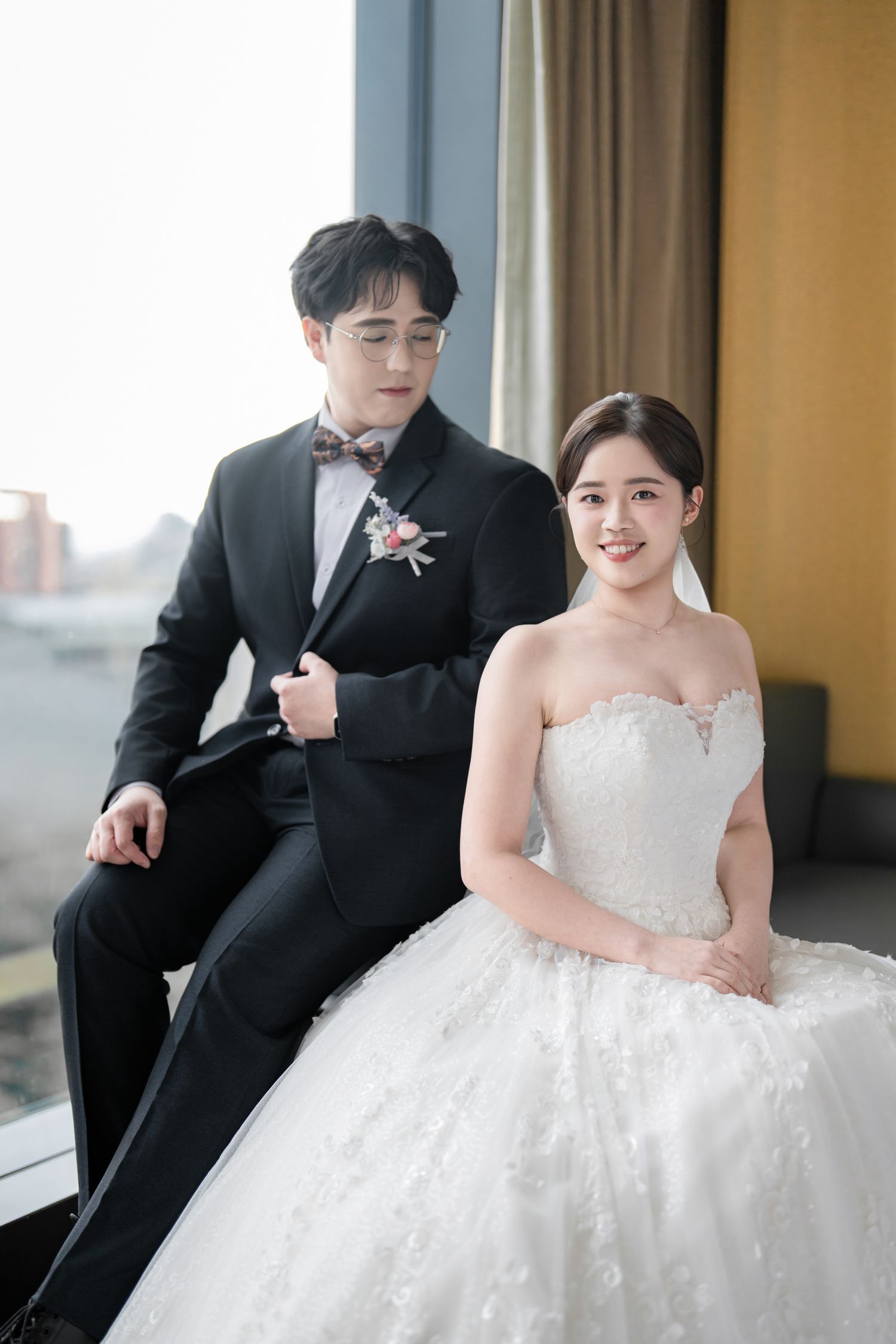 A wedding couple poses for romantic photos in a hallway, with the bride in a white lace gown and groom in black suit.