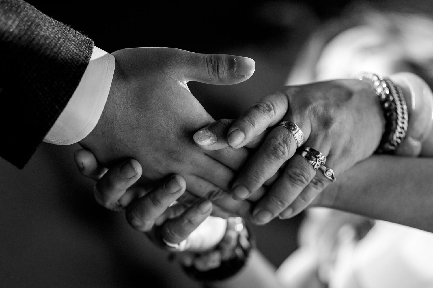 Black and white photo of multiple hands joined together, featuring rings and bracelets, symbolizing unity.