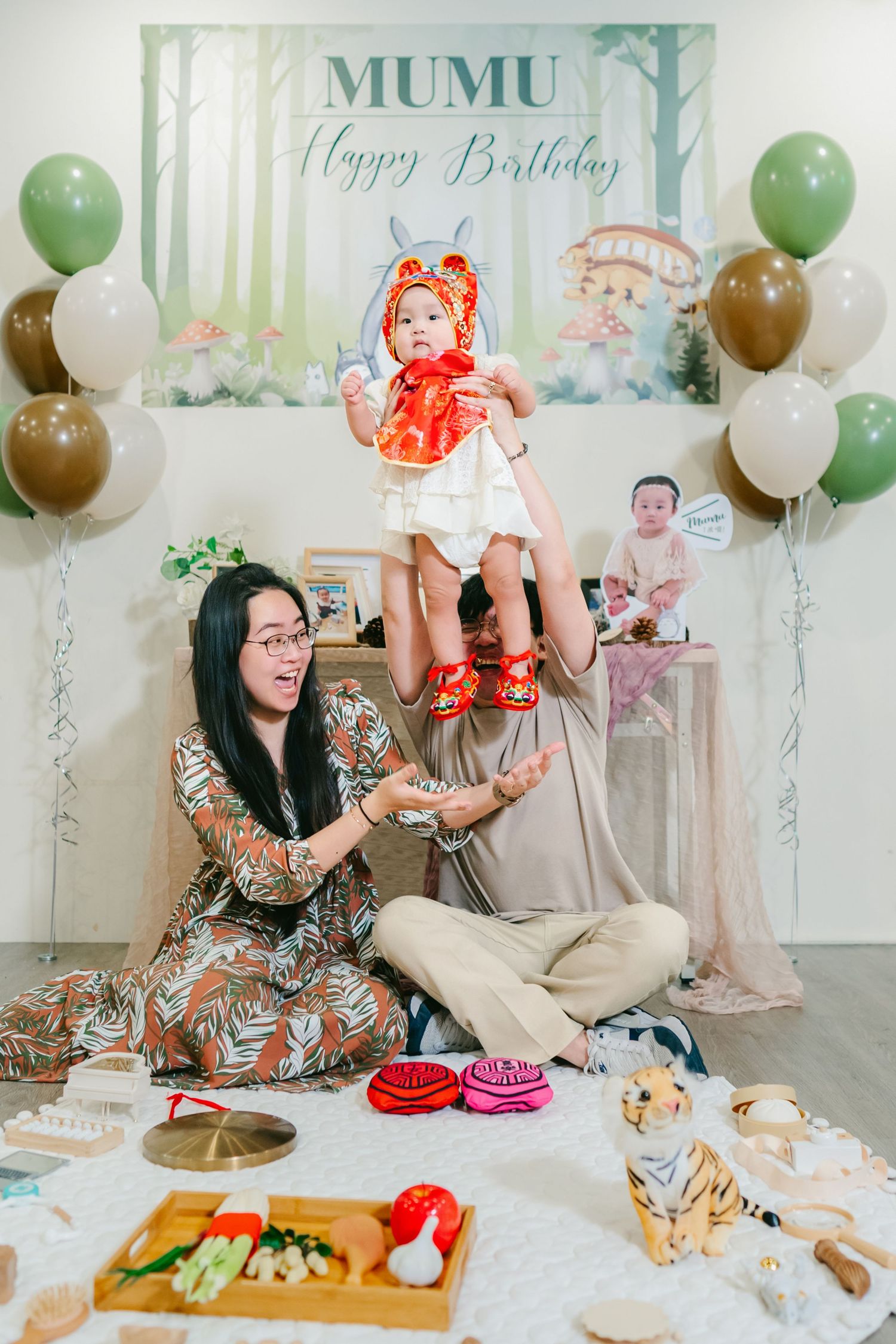 A birthday party setup with forest-themed backdrop, colorful balloons, and snacks arranged on a picnic blanket.
