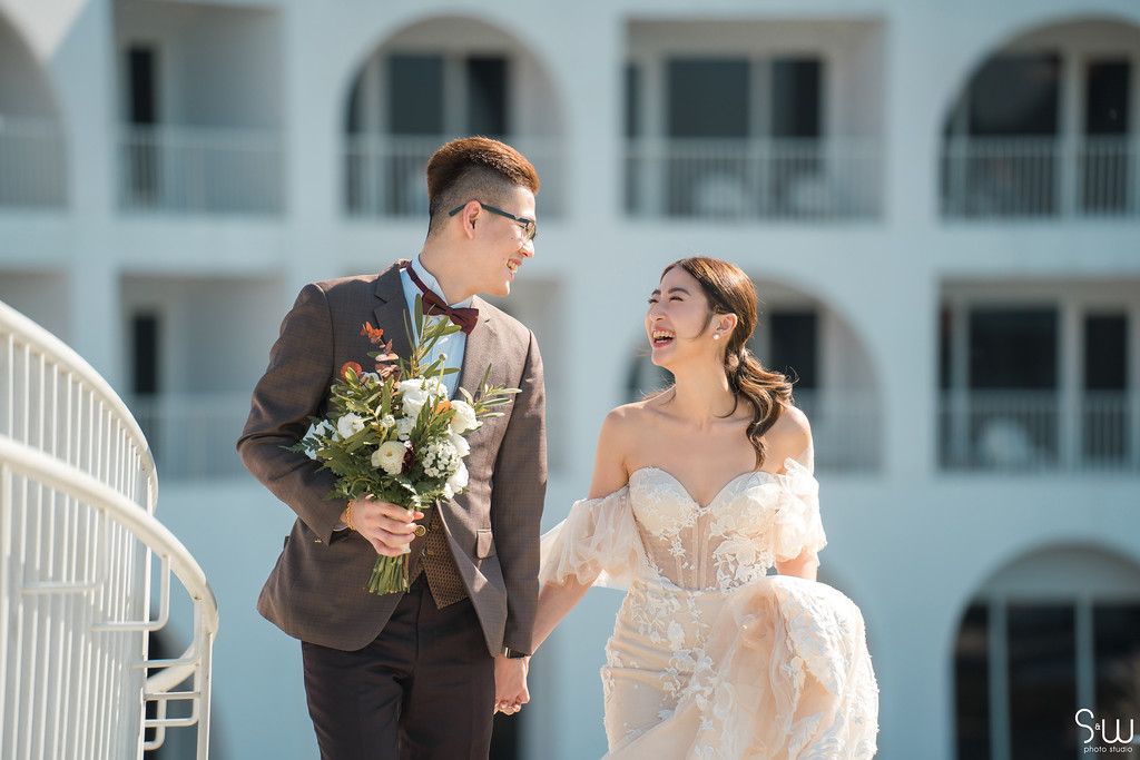 A couple shares a joyful moment together on a white balcony with beautiful resort architecture.