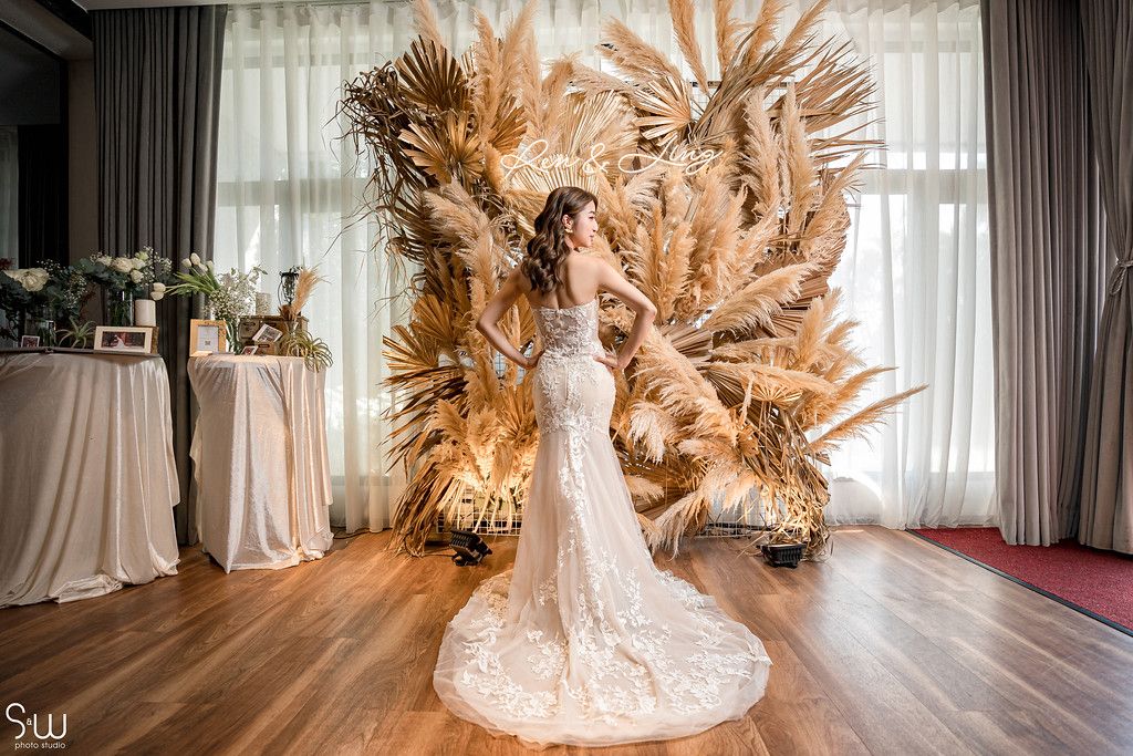 Wedding dress displayed in front of stunning dried pampas grass backdrop installation in light-filled room.