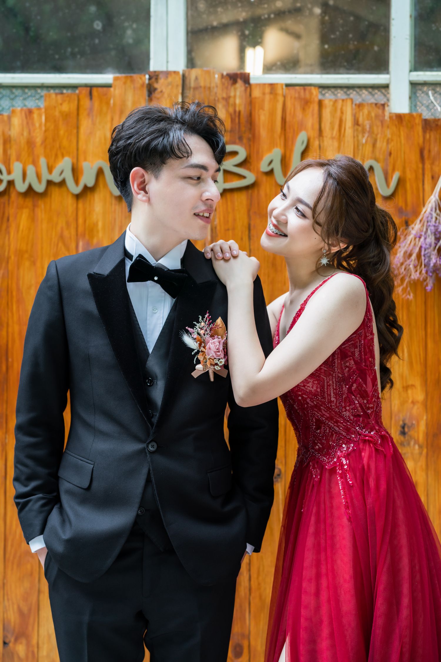 Romantic outdoor photoshoot with formal attire against rustic wooden wall backdrop.