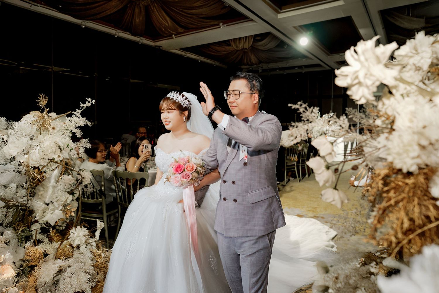 A couple shares a romantic moment during their wedding reception surrounded by elegant white floral decorations.
