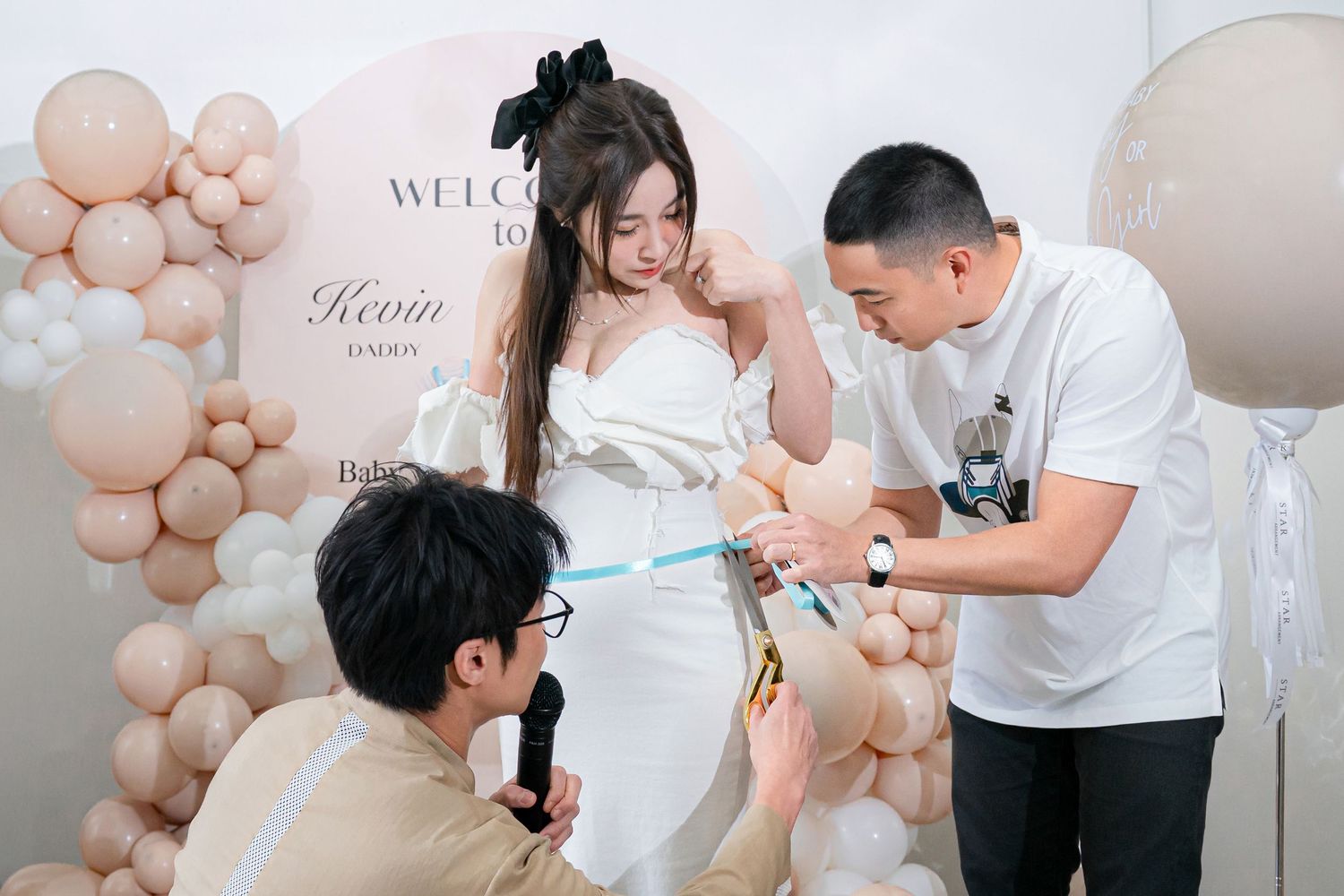 Family members gather around balloon decorations at a pink and white themed celebration party.