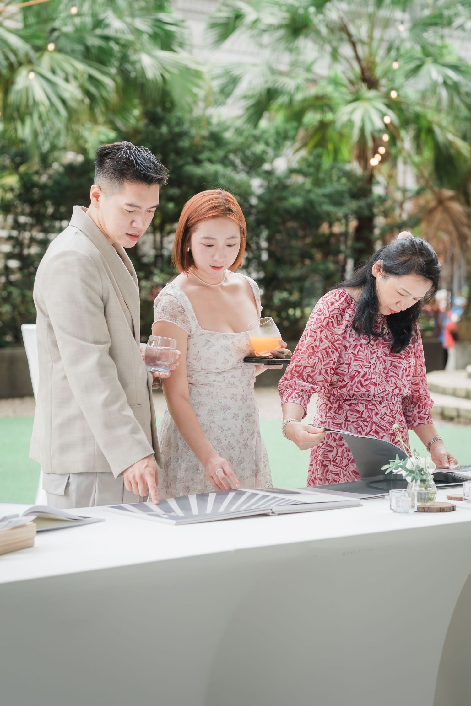 Three people sign paperwork together at a white table outdoors during a formal event with palm trees in the background.