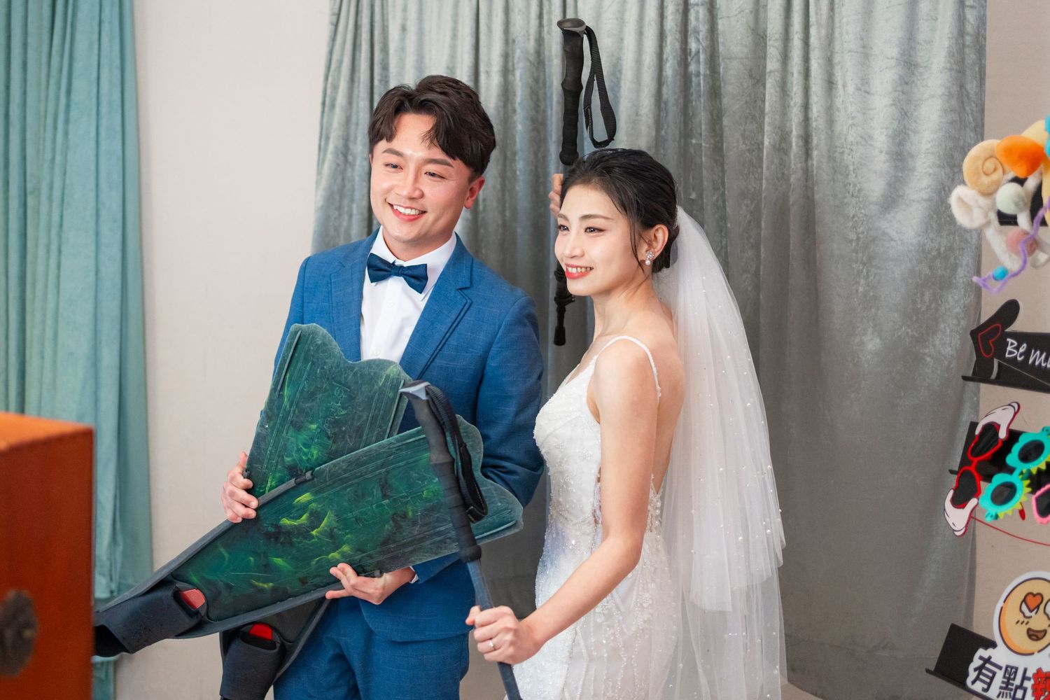A couple in formal wedding attire smile while holding a decorative green photo album during their photo session.