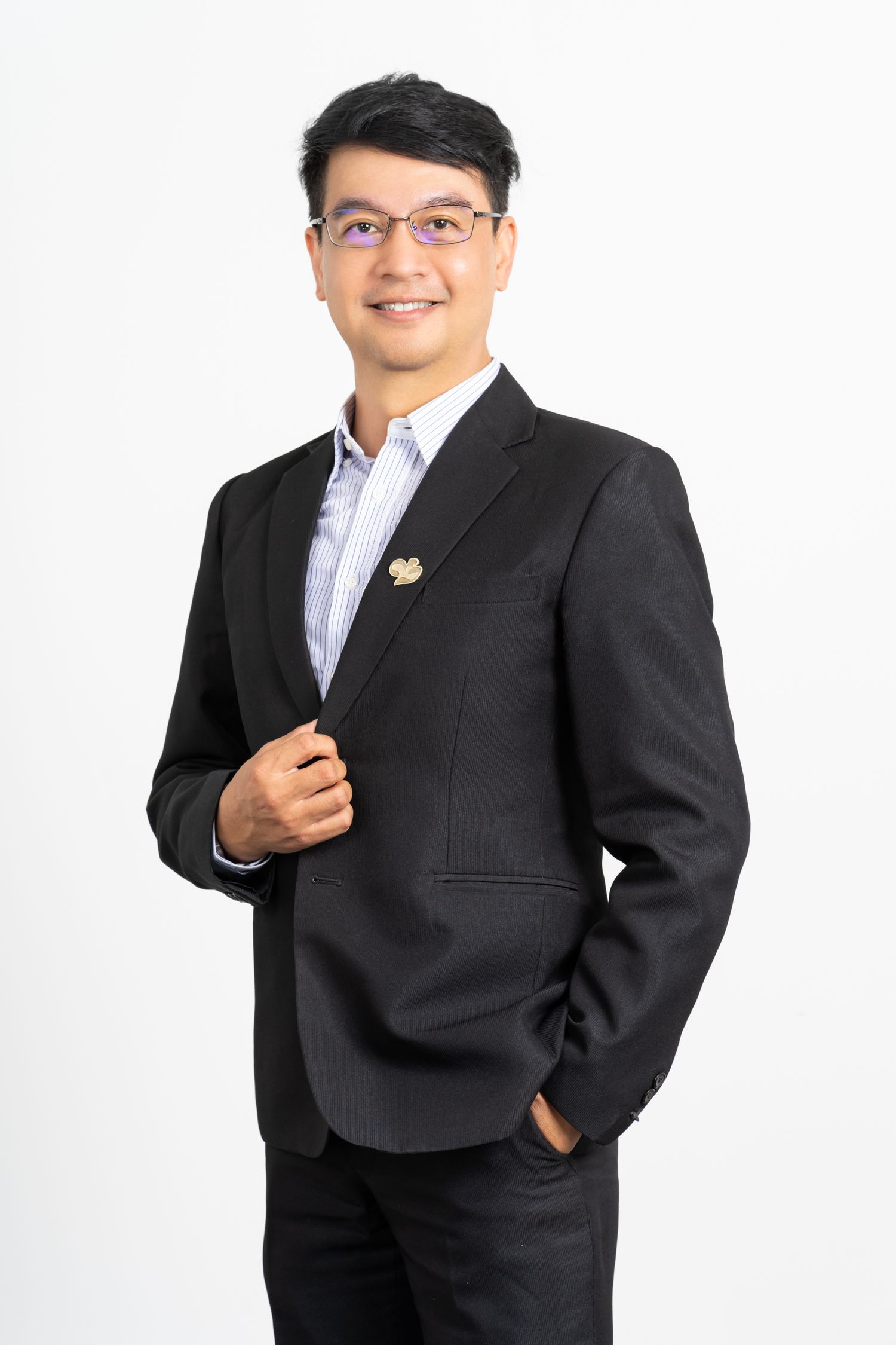Person in dark blazer and glasses poses confidently against white background in business attire.