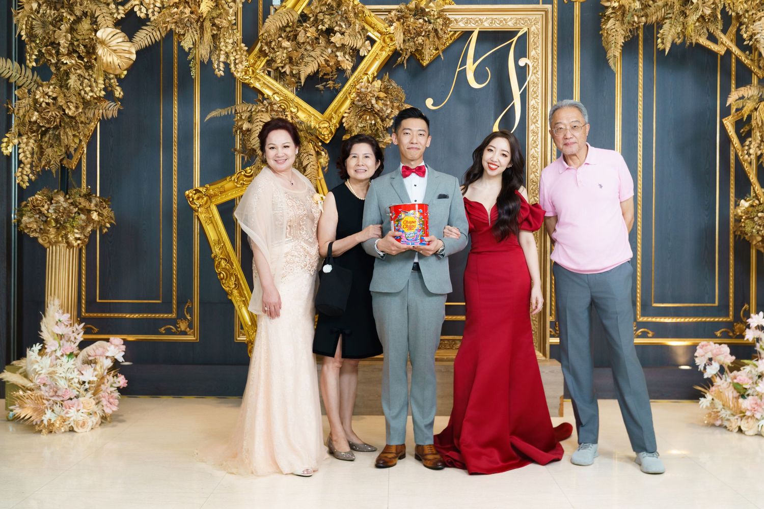 A group of people in formal attire pose together against an ornate blue and gold backdrop at a special event.