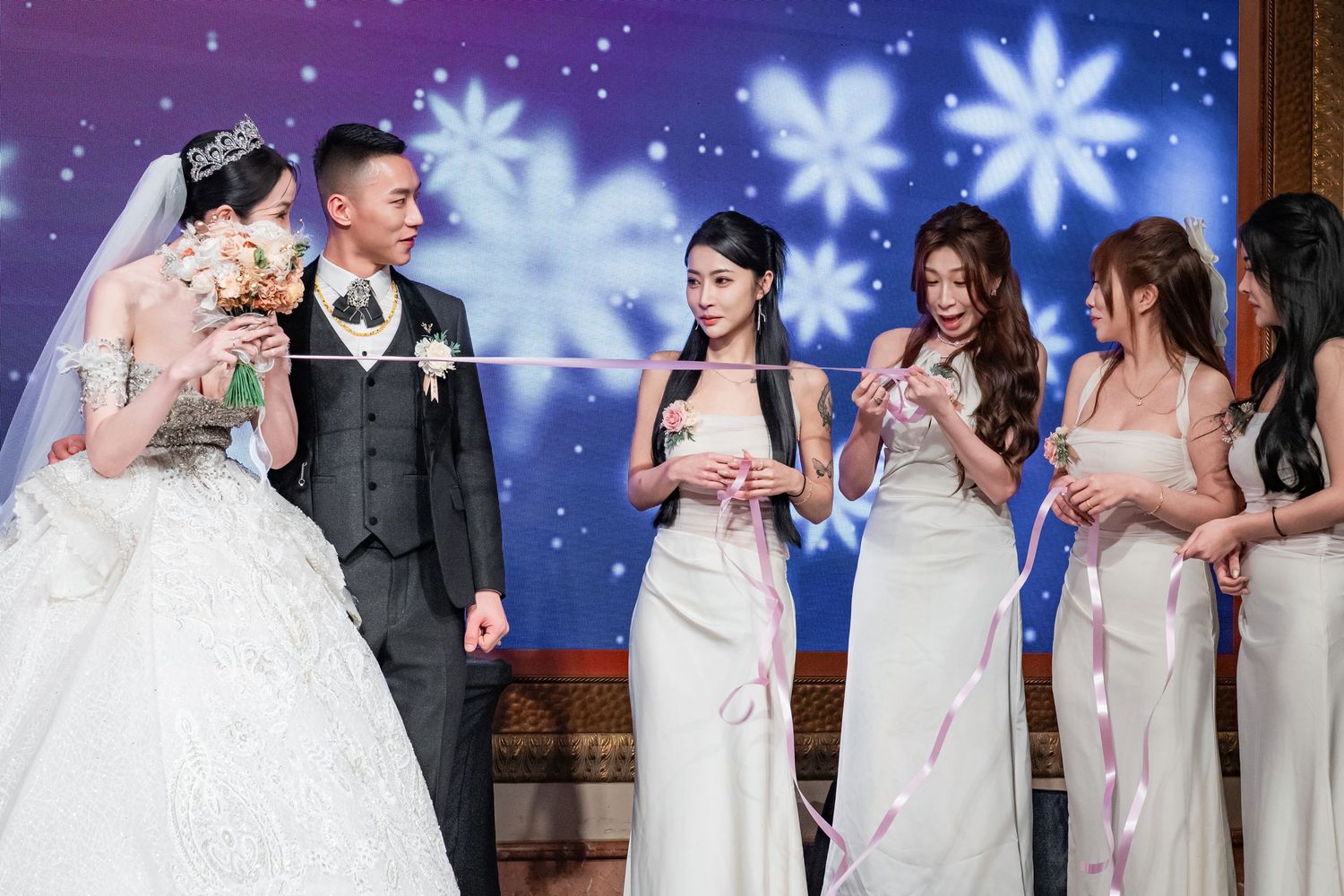 A wedding celebration scene with a bride in white gown and wedding party members against a backdrop of blue snowflakes.