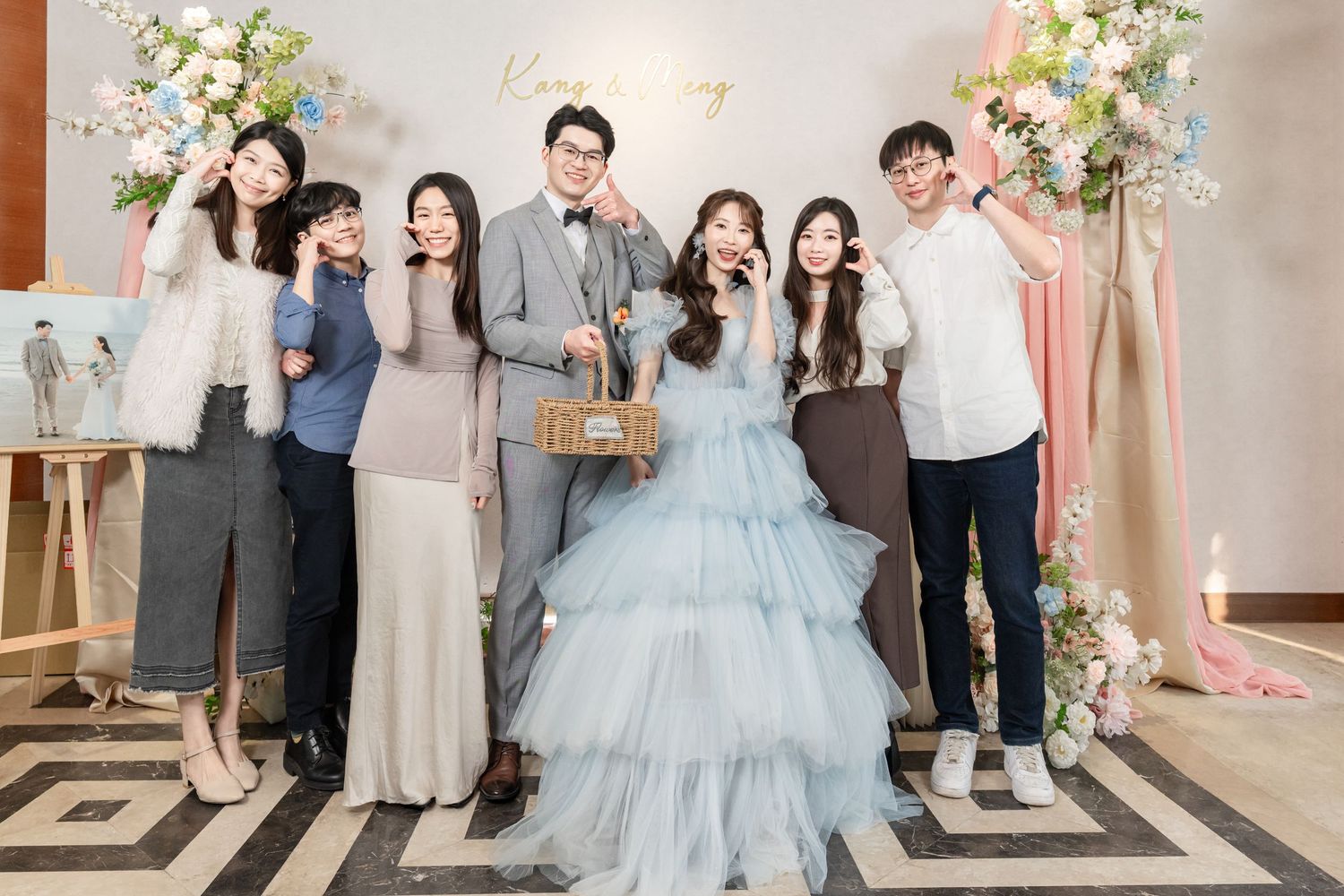 Wedding party poses together in formal attire with blue gown and floral decorations at elegant indoor venue.