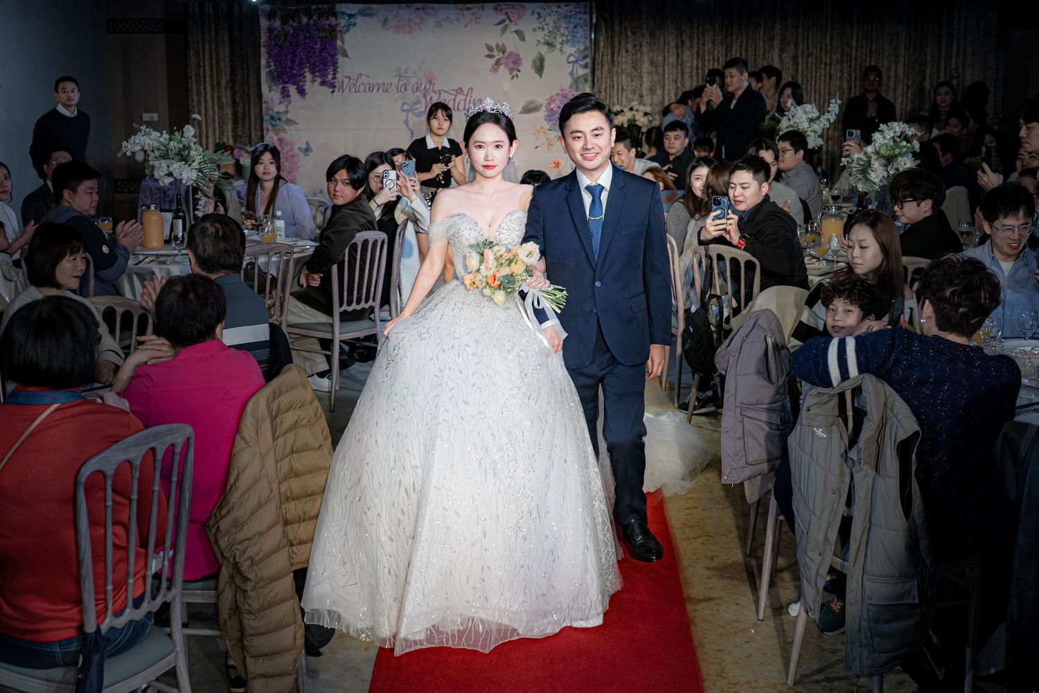 Wedding ceremony guests gather in an elegant venue with floral decorations and formal attire.