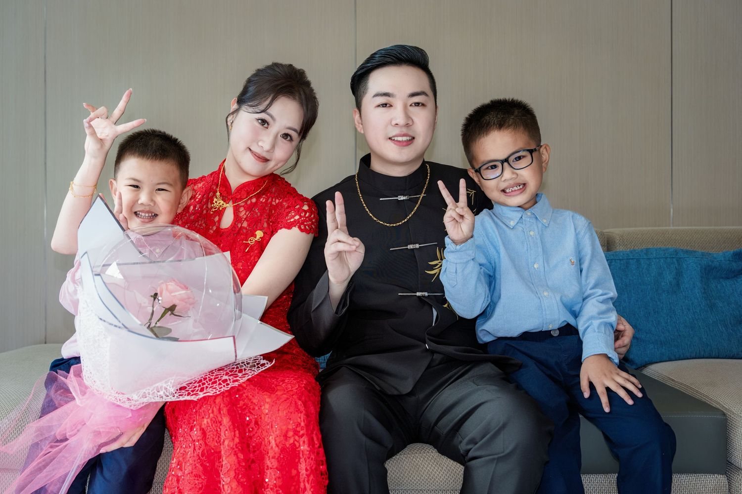 A family group in festive attire sits together on a blue couch making peace signs and smiling for the camera.