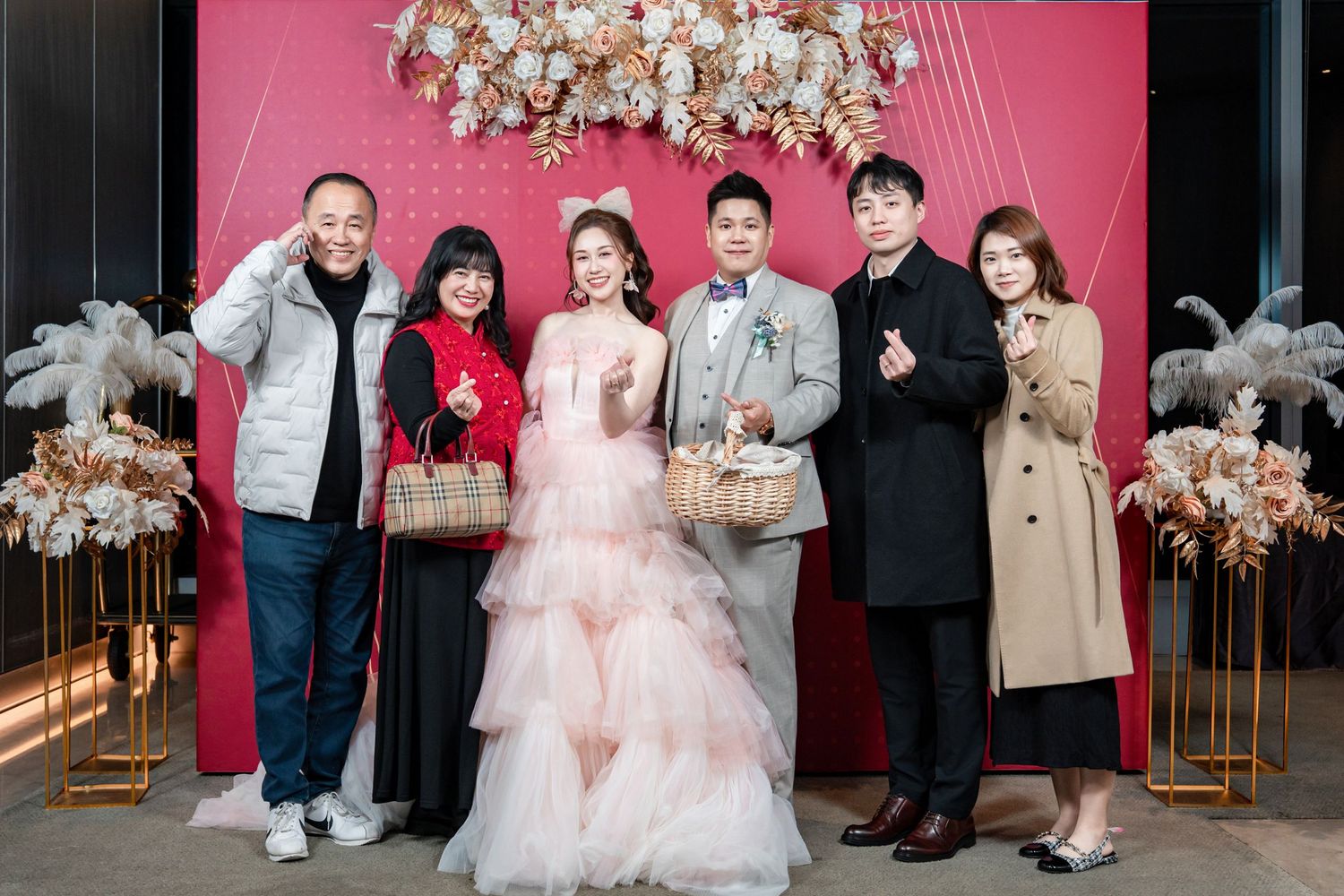 Group photo session with pink backdrop and floral decorations at a celebratory event.