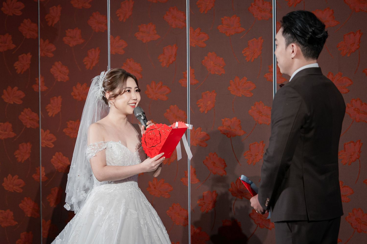 A wedding couple poses playfully with red fans against a dark floral wallpaper background in a series of photos.
