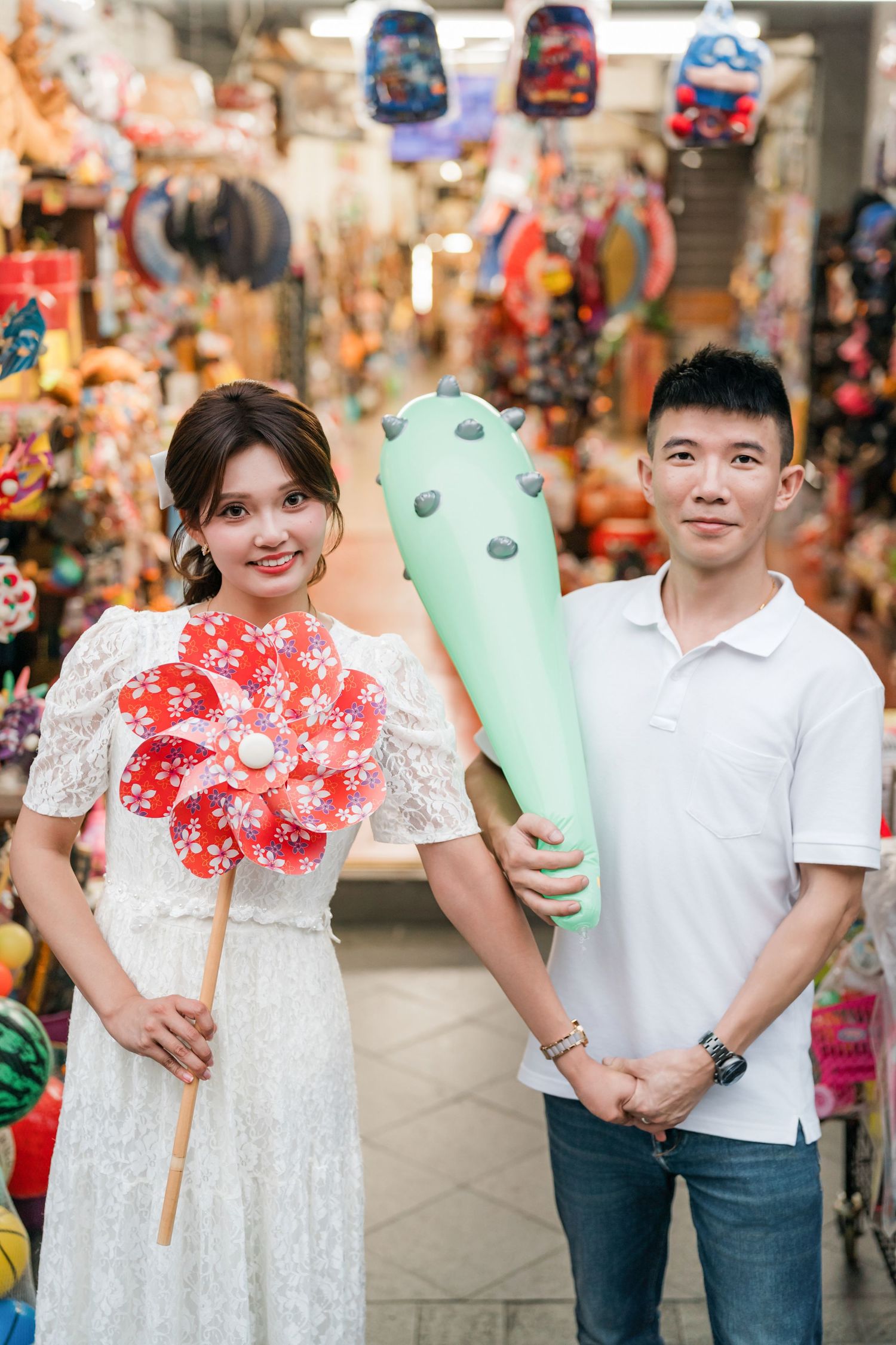 A group wearing white outfits holds decorative mushroom-shaped props at a market or shopping area.
