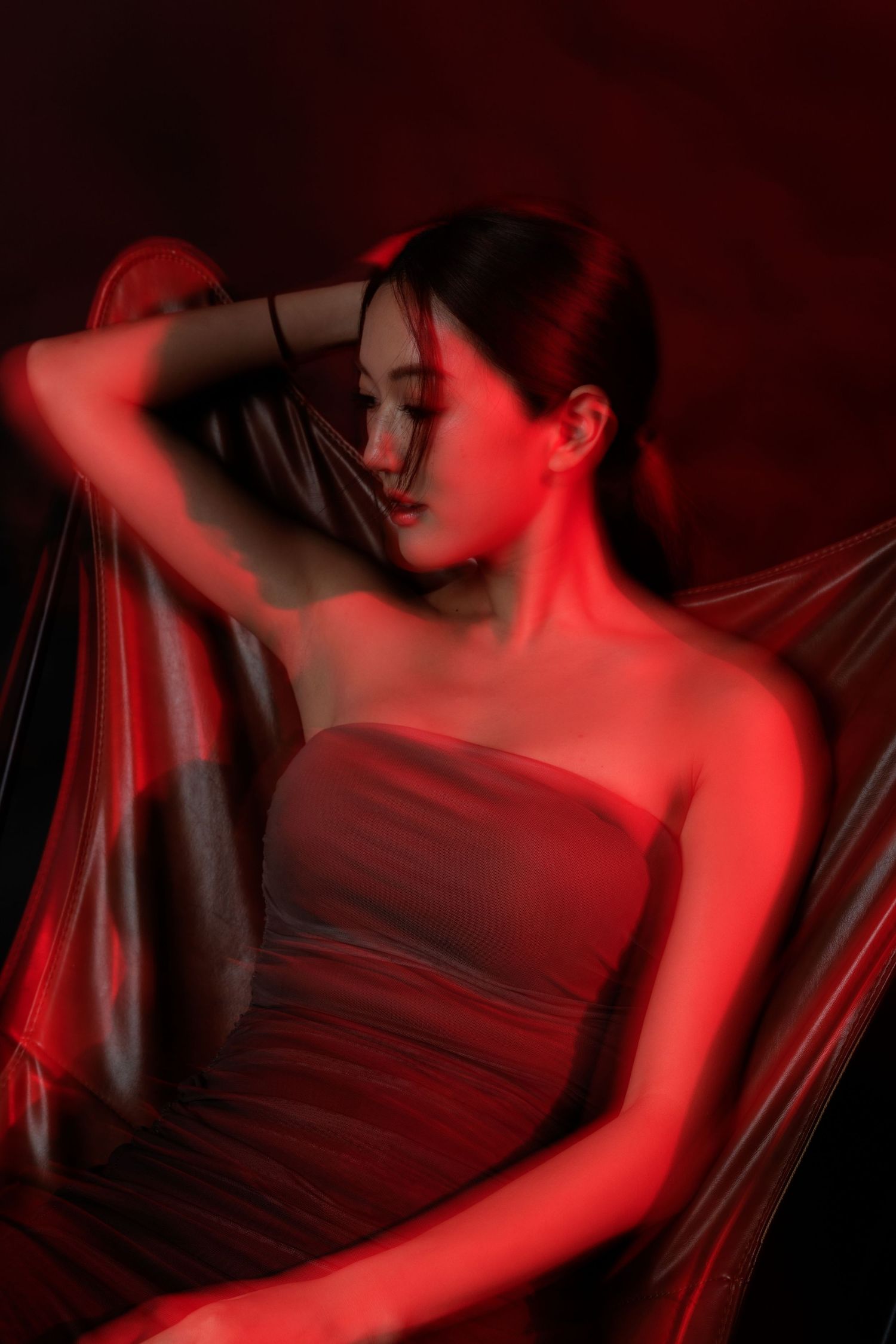 A woman in a strapless dress poses gracefully under dramatic red lighting against a dark background.