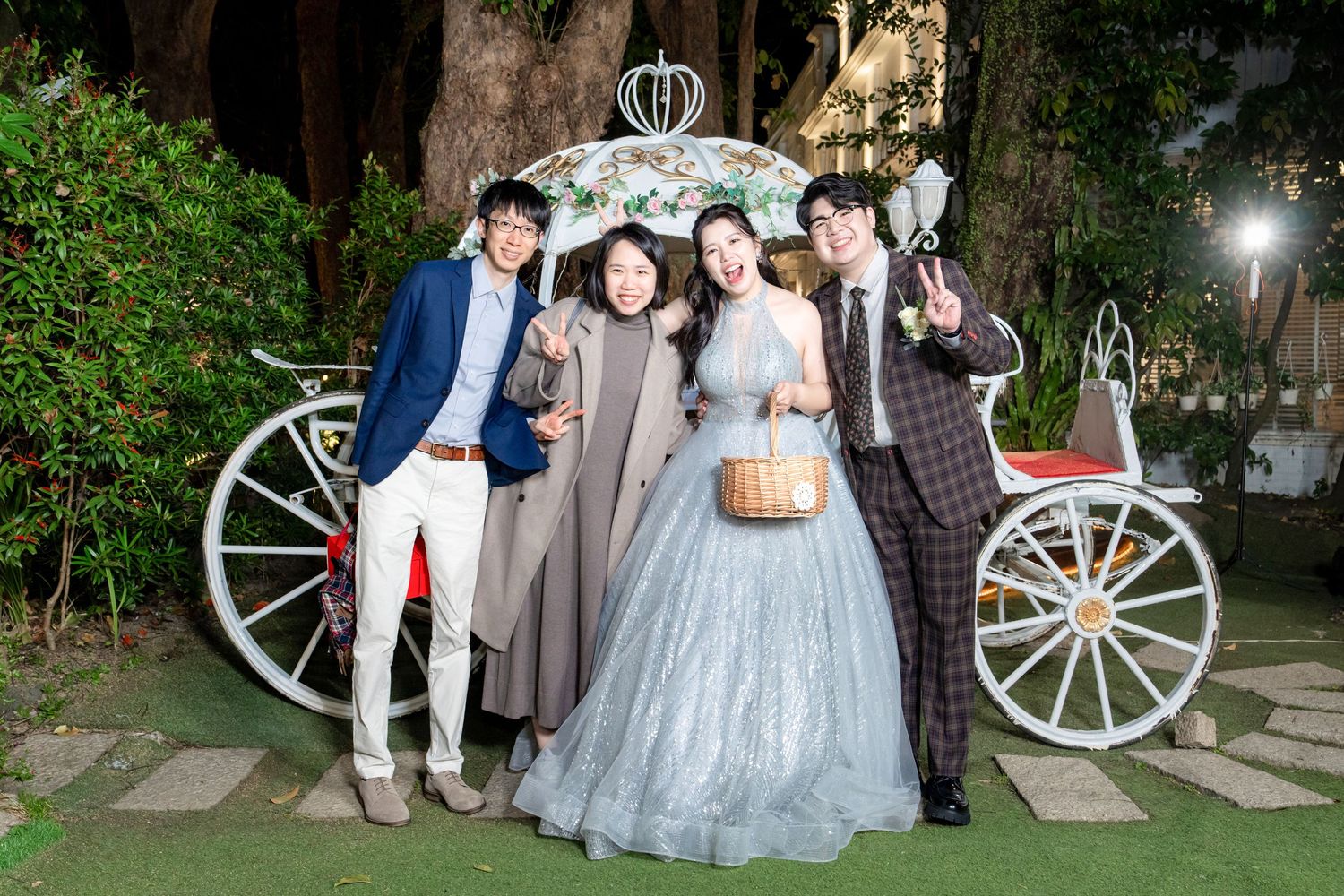 A group poses together at an outdoor garden wedding venue with decorative white wagon wheels in the background.