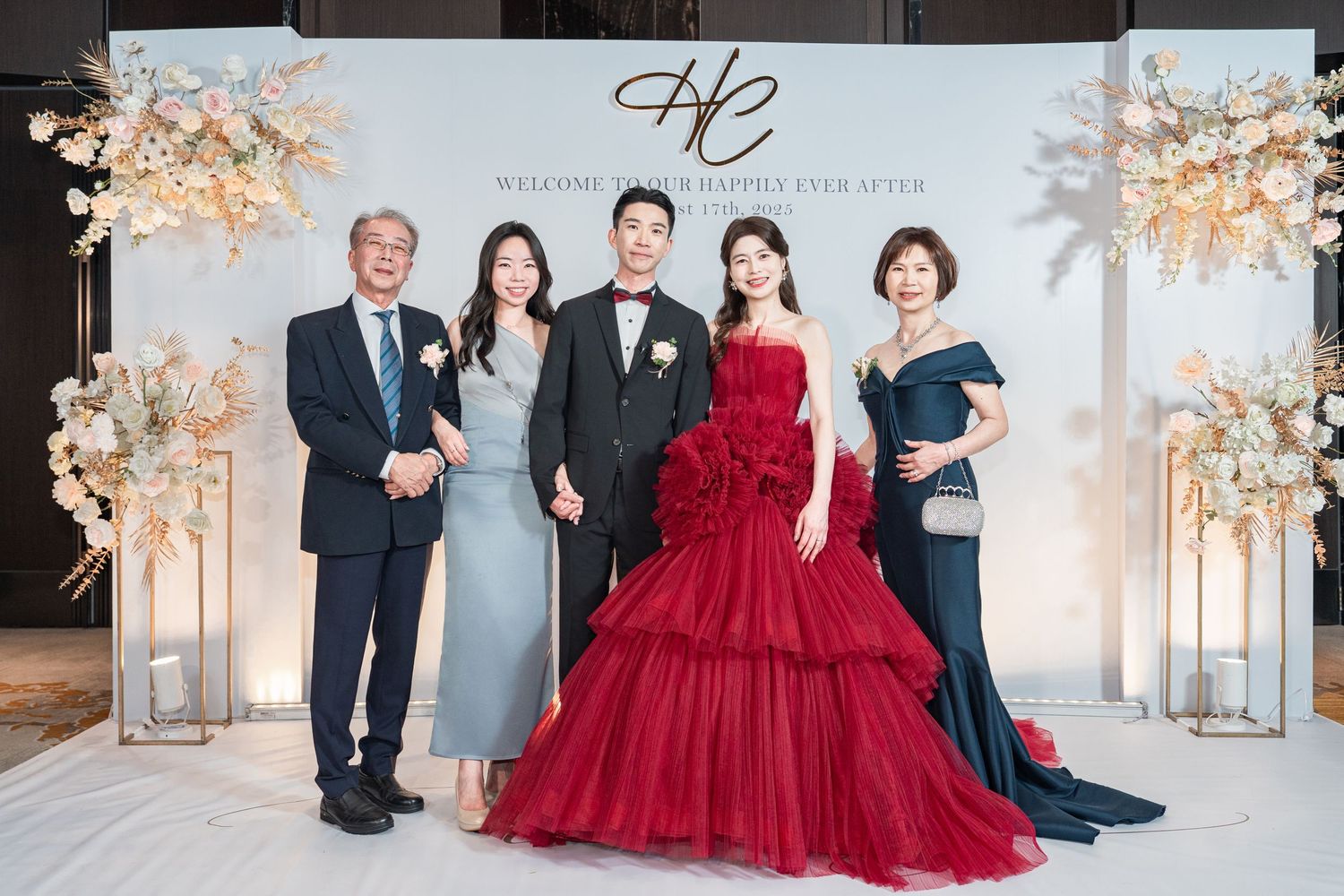 A group in formal attire poses in an elegant white room with soft floral arrangements and decorative accents.