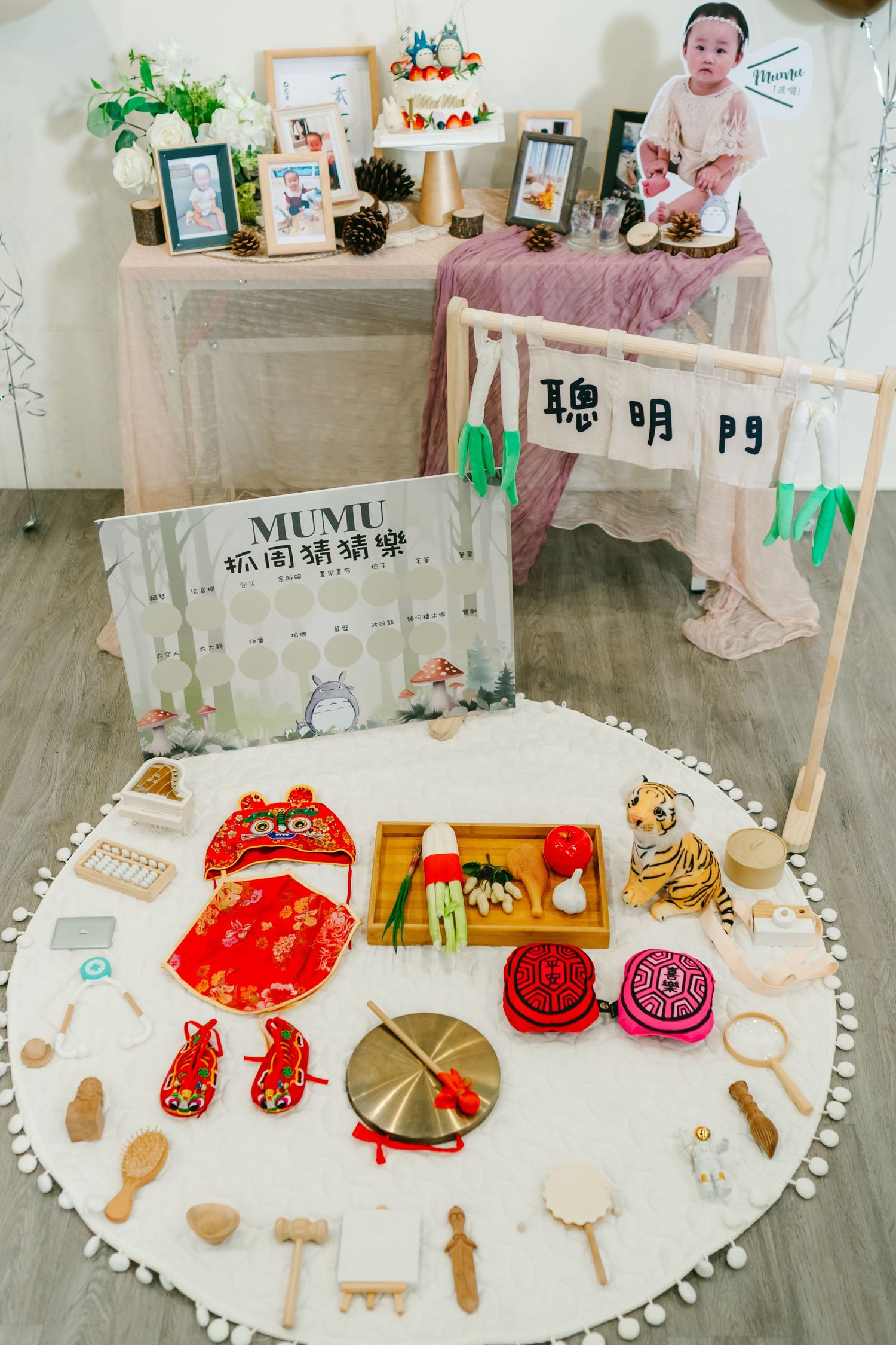 Indoor celebration setup with Chinese decorative elements, toys and snacks arranged on a white round mat with pink decor details.