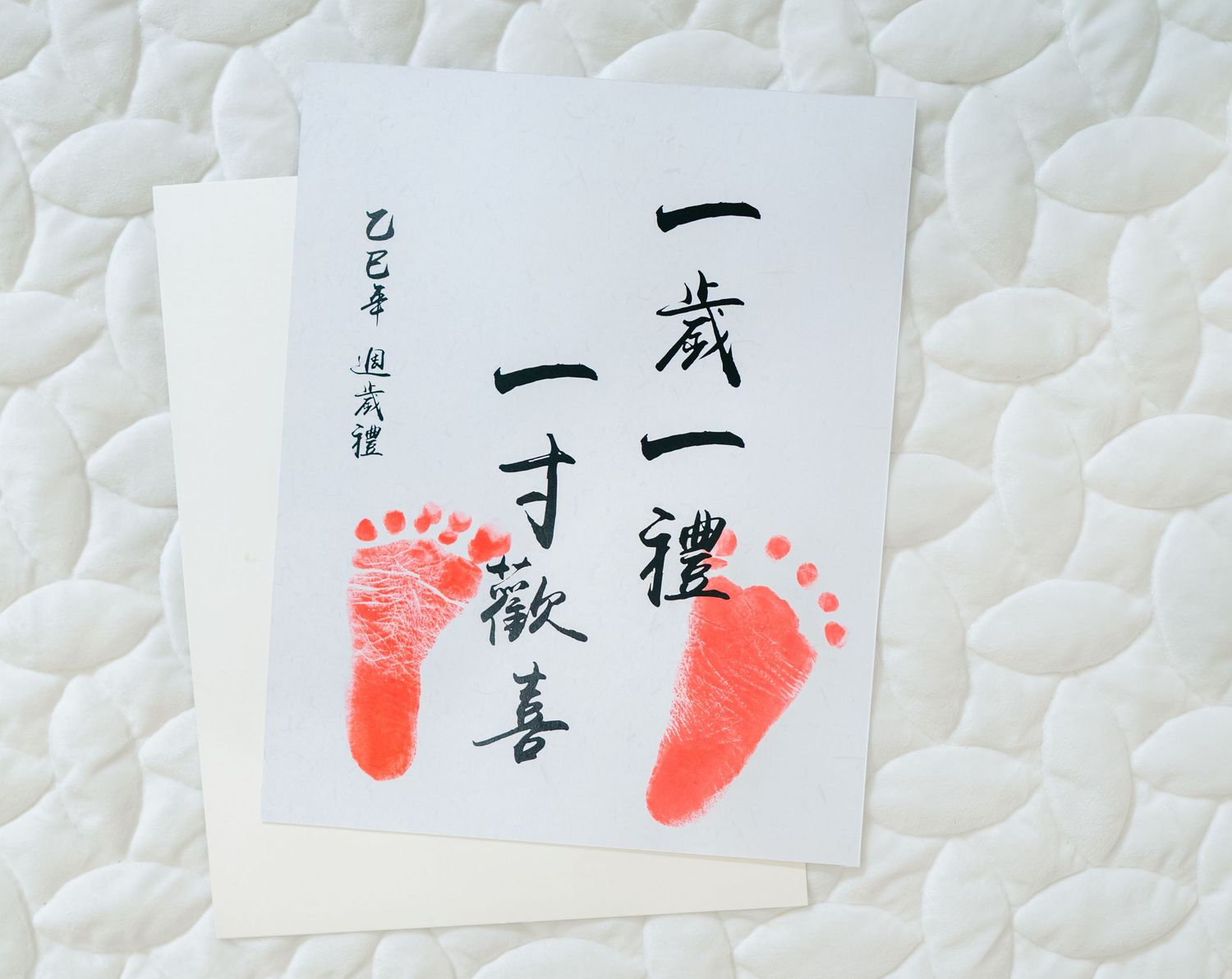 Japanese birth certificate or celebration document with red baby footprints and calligraphy on white paper.