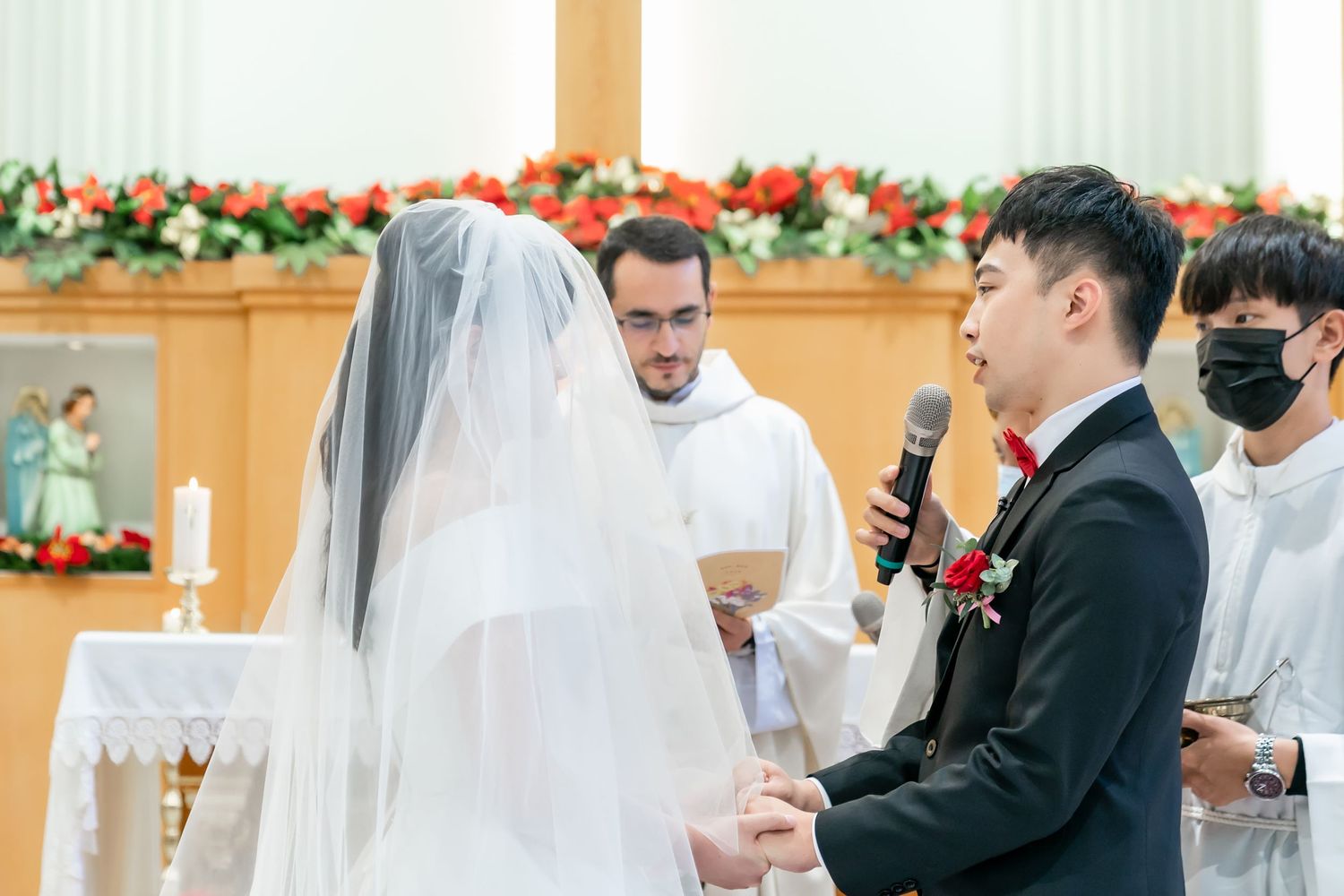 Catholic wedding ceremony taking place in a church with floral decorations and white altar décor.