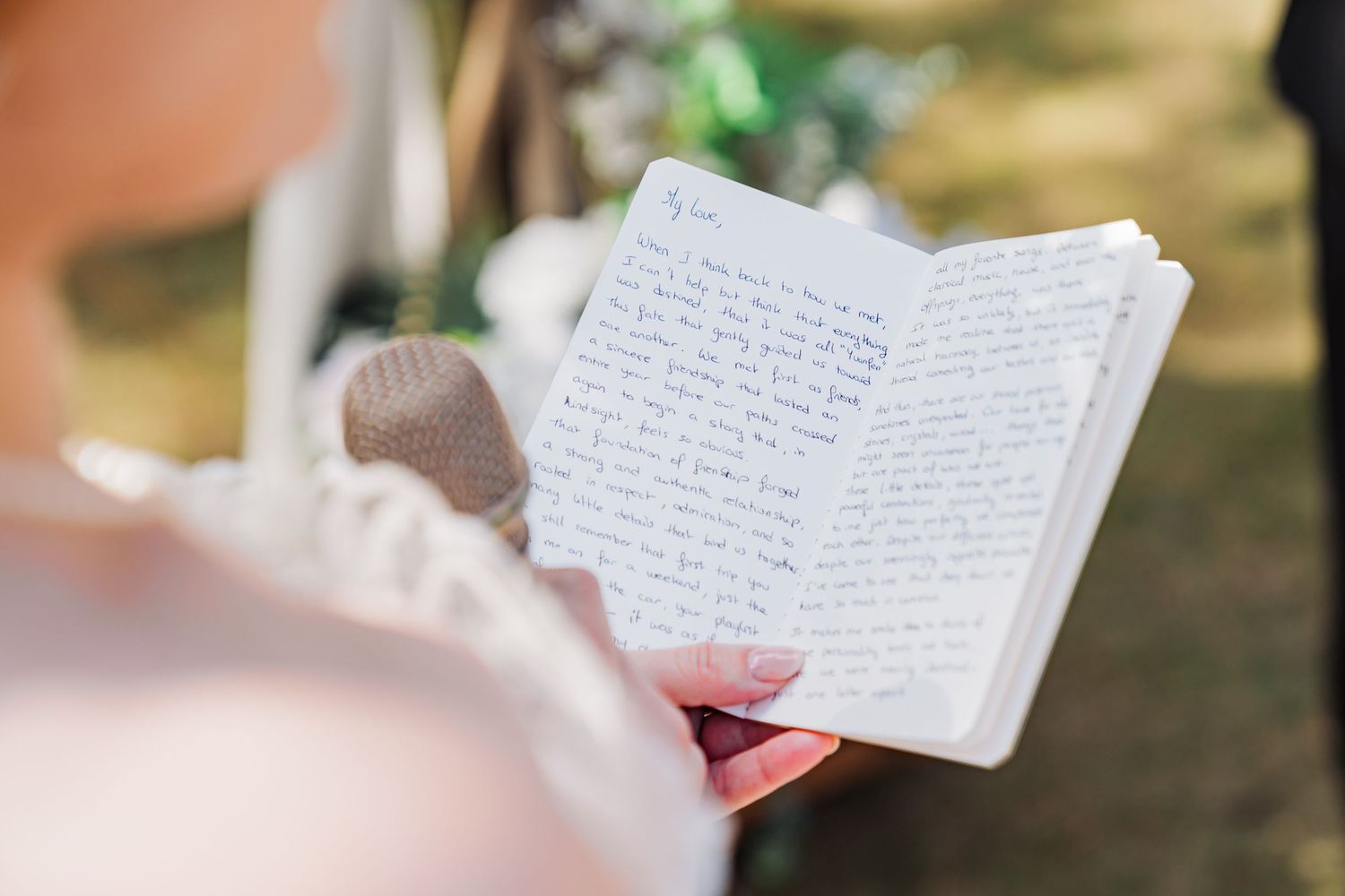 Open handwritten notebook being read during outdoor wedding ceremony.
