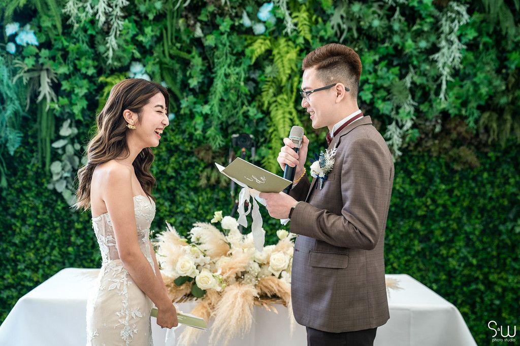 Couple exchanges vows in front of a verdant wall during their outdoor wedding ceremony.
