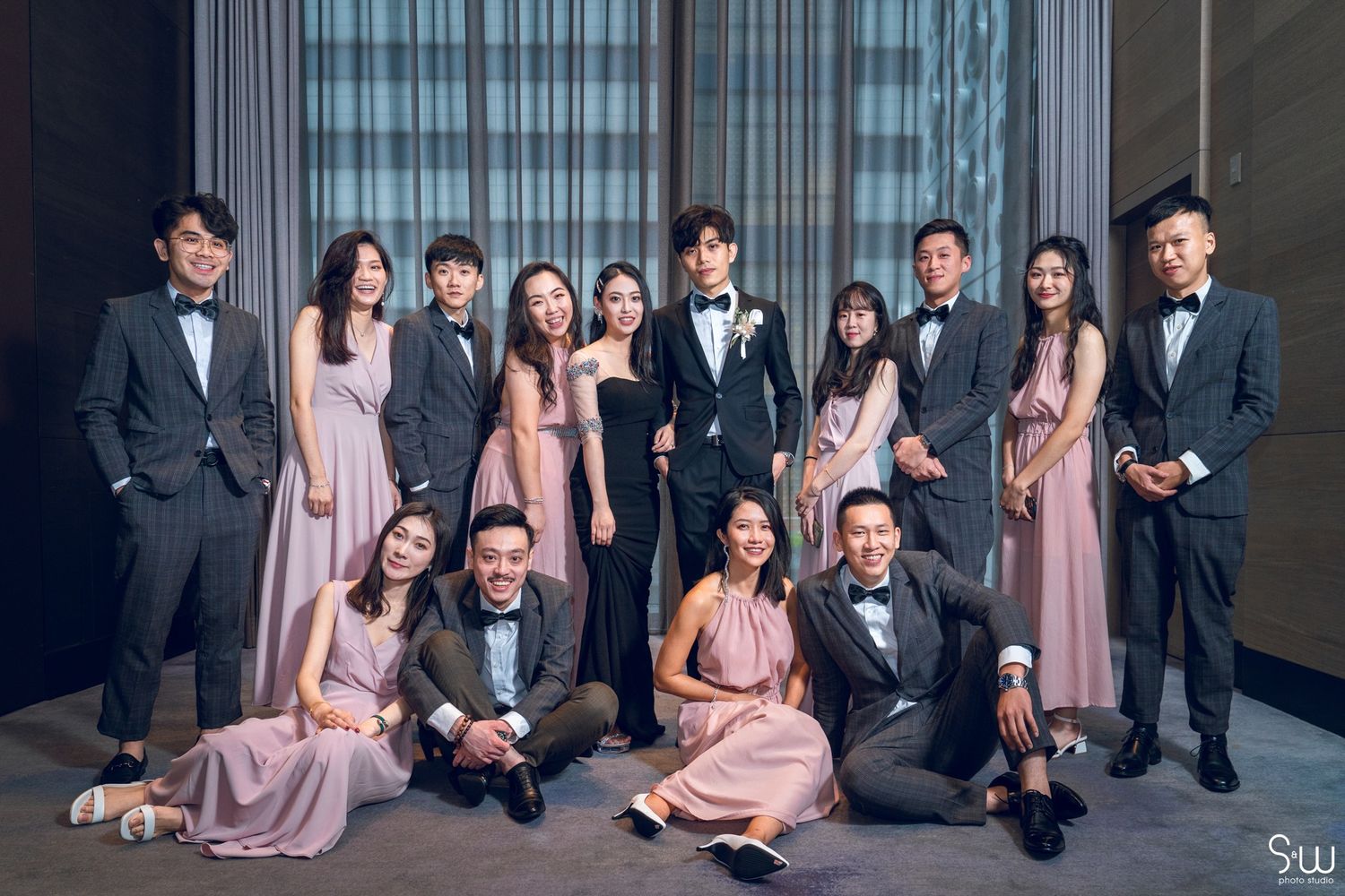 Wedding party members in suits and pink dresses pose together in an elegant hotel setting.