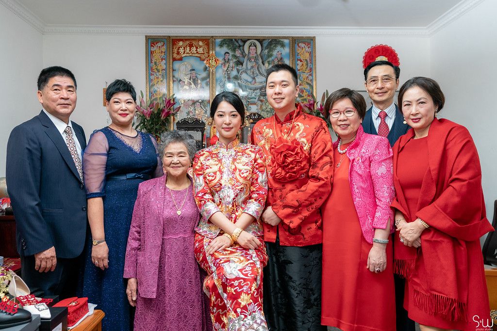 Family gathering in formal attire with traditional Chinese wedding decorations.