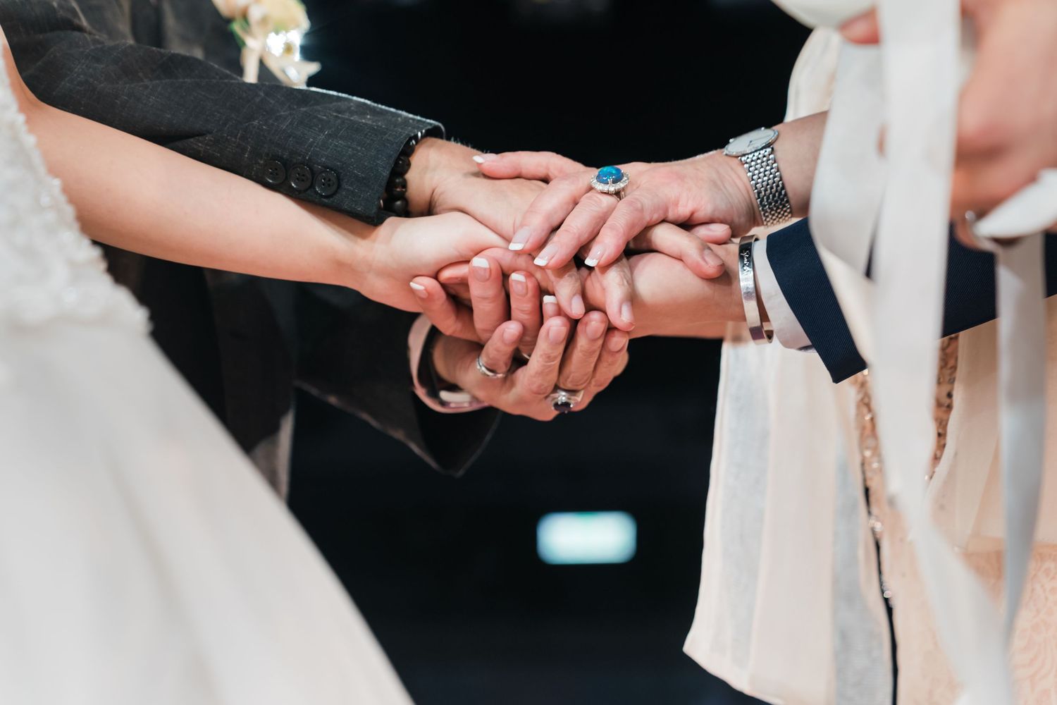 A group of hands stacked together in unity during a formal gathering or celebration.