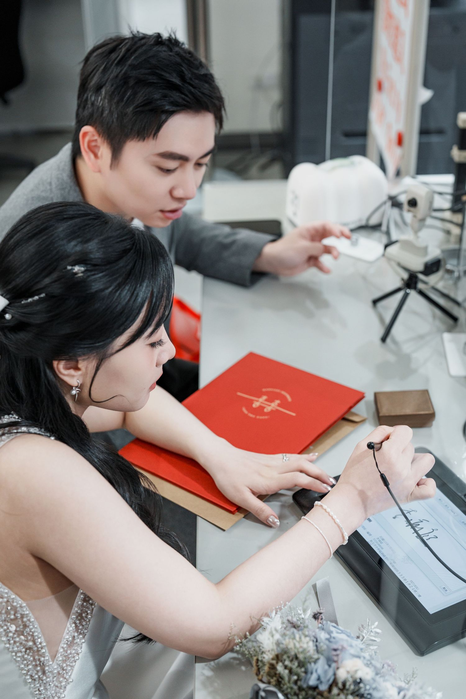 A person practices calligraphy writing with a brush pen on paper next to a red book in a studio setting.
