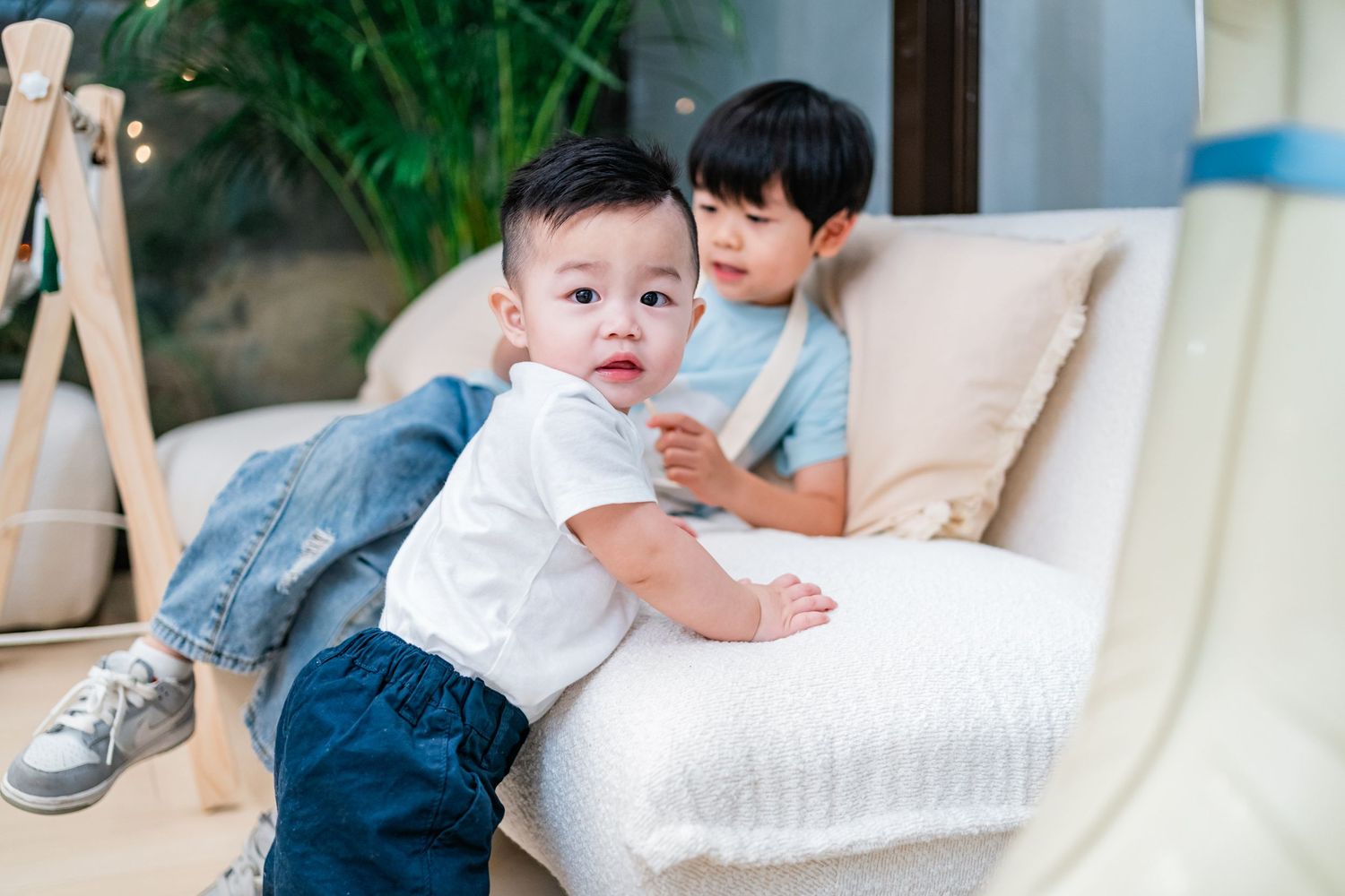 Two children play together on a white couch in a bright indoor setting.