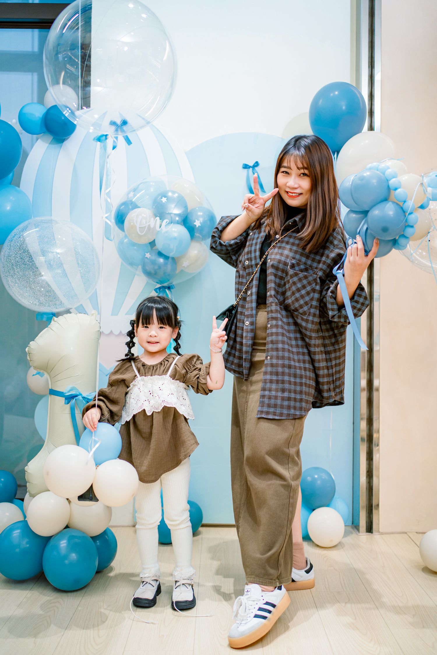 A child and caregiver play together in a room decorated with blue and white balloons for a celebration.