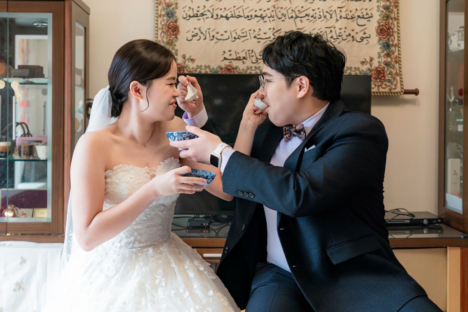 A couple in wedding attire shares a toast with wine glasses during their celebration.