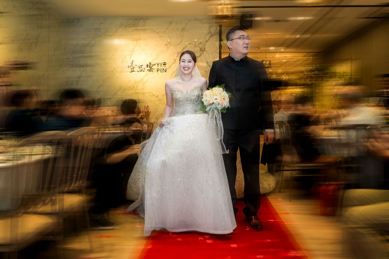 Blurred motion shot of dancing at a wedding reception with warm ambient lighting and a red carpet.