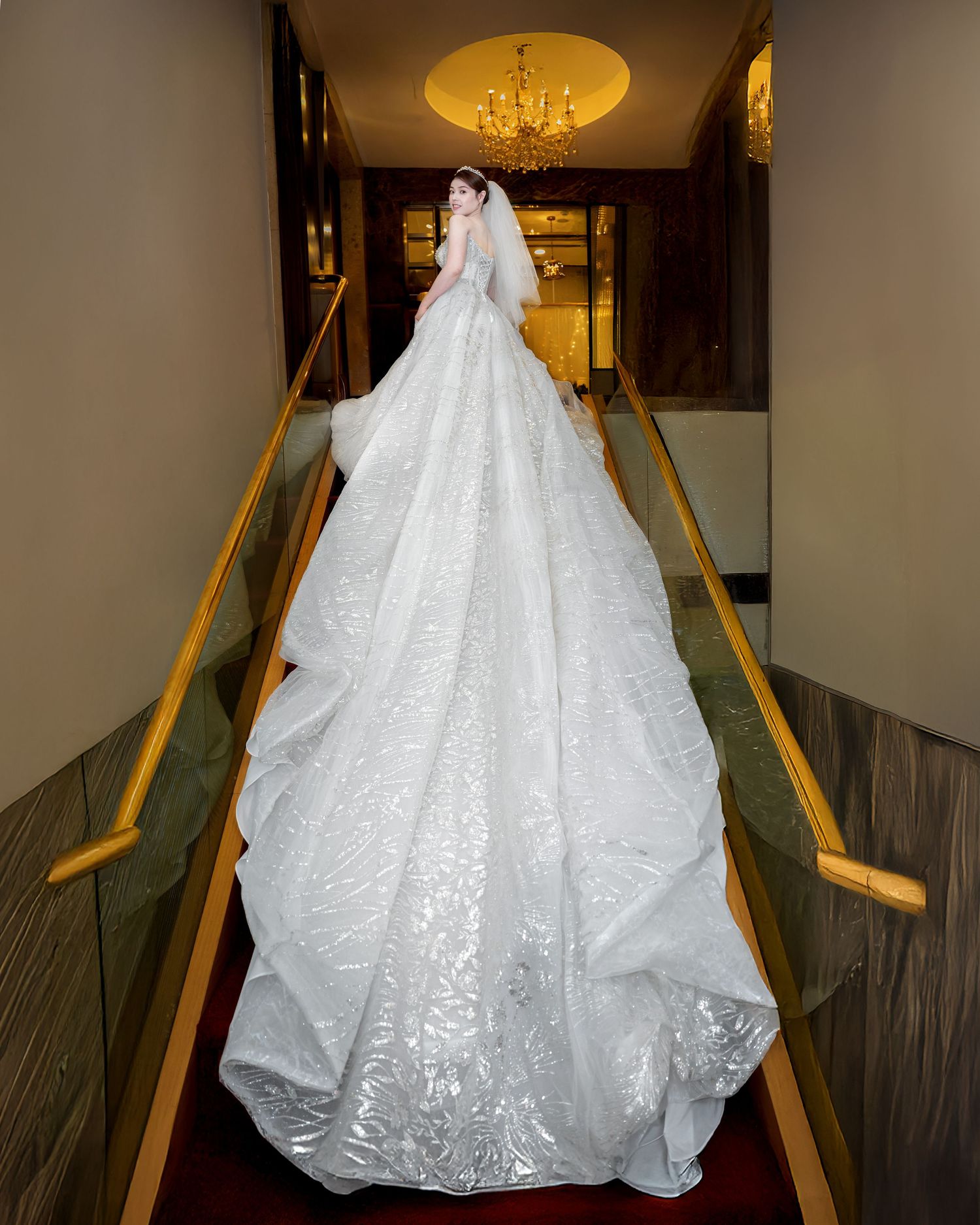 A stunning white wedding gown with intricate lace details and a flowing train displayed on a carpeted staircase.