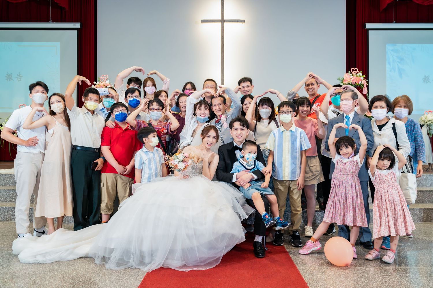 Fun group wedding photo with guests making heart gestures on church steps.