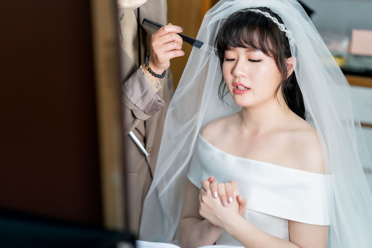 Close-up of a serene bride in white off-shoulder gown and veil during preparations.
