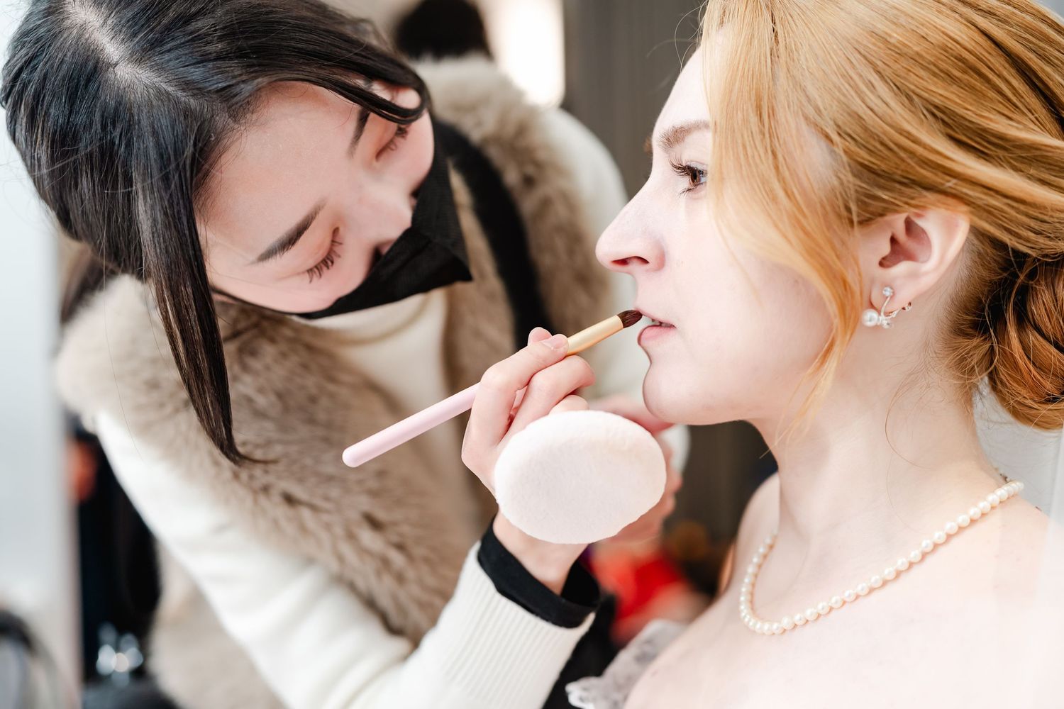 Detailed makeup application being performed in an elegant bridal preparation setting.