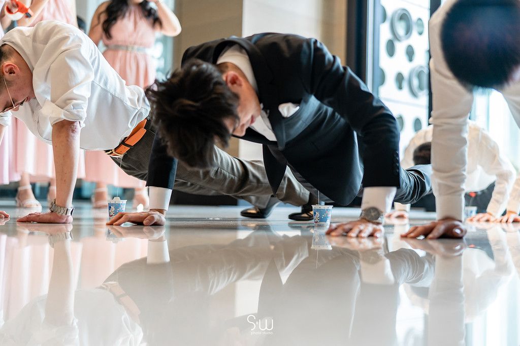 Wedding party members in formal attire crawling on a reflective floor.