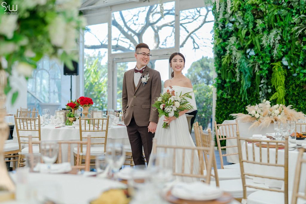 A couple enters elegant wedding reception venue with floral decorations and golden chairs.
